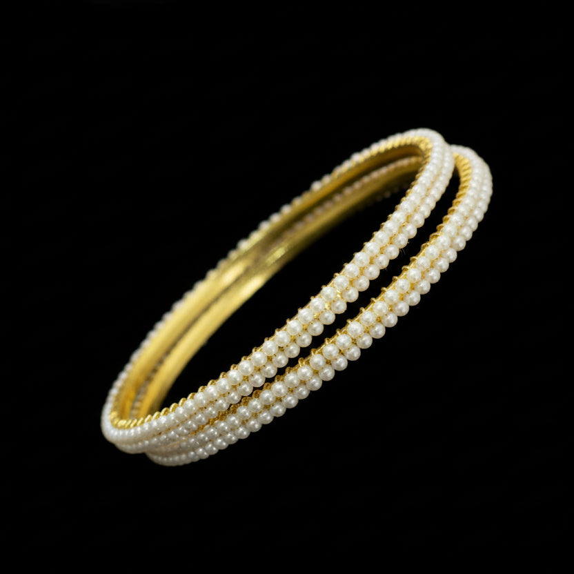 Gold and pearl bracelet on a black stand with 'Saheli' branding.