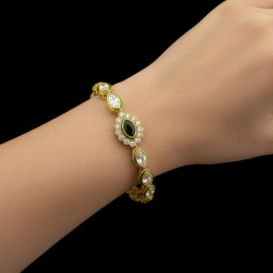 Gold bracelet with green accents on a dark background, featuring the brand 'Saheli'.
