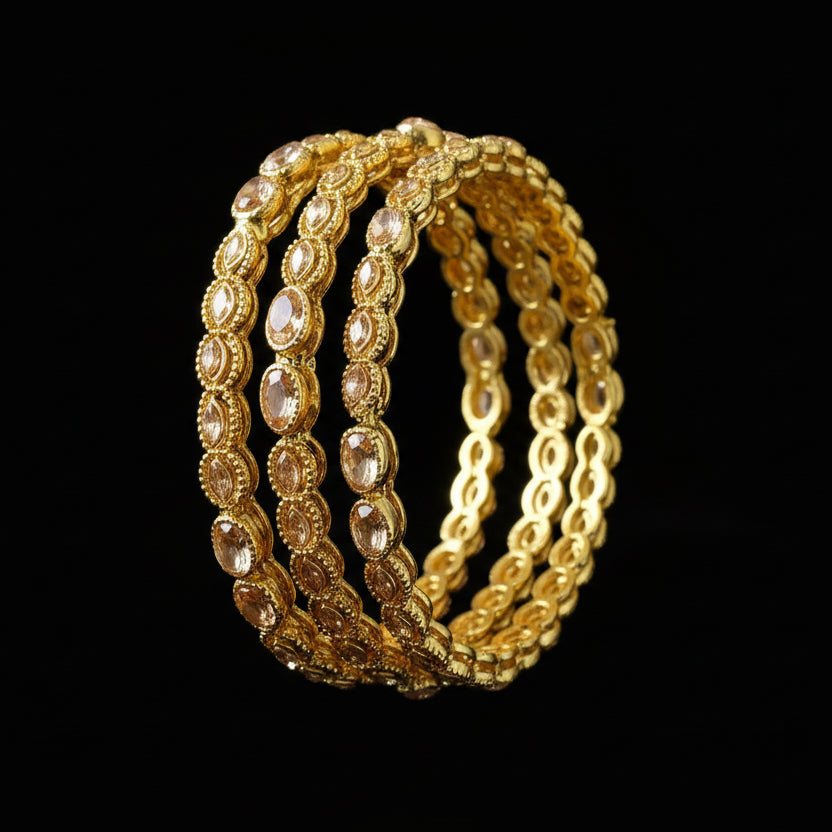 Gold bangles with gemstones on a gray background, featuring the brand 'Saheli'.