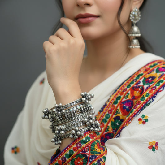 Silver bangles with decorative elements on a gray stand, branded 'SAHELI'.