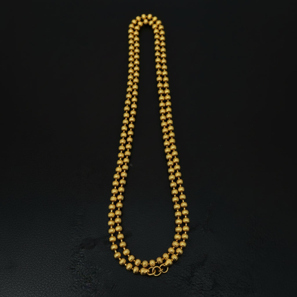 Gold beaded necklace with a tag on a black textured surface