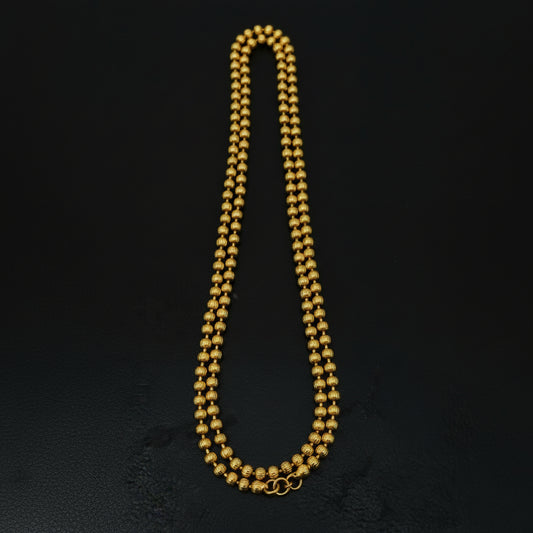 Gold beaded necklace with a tag on a black textured surface