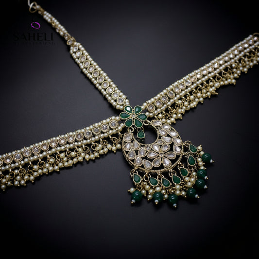 Ornate necklace with green gemstones on a dark background, featuring the brand 'Saheli'.