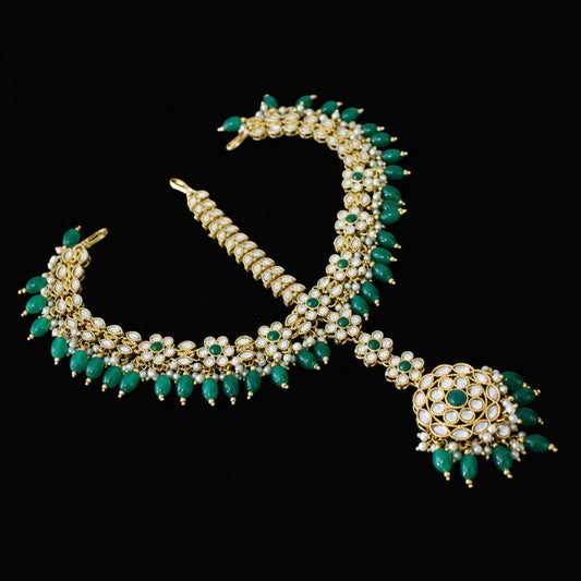 Gold and green necklace with pendant on a dark background, featuring the brand 'Saheli'.