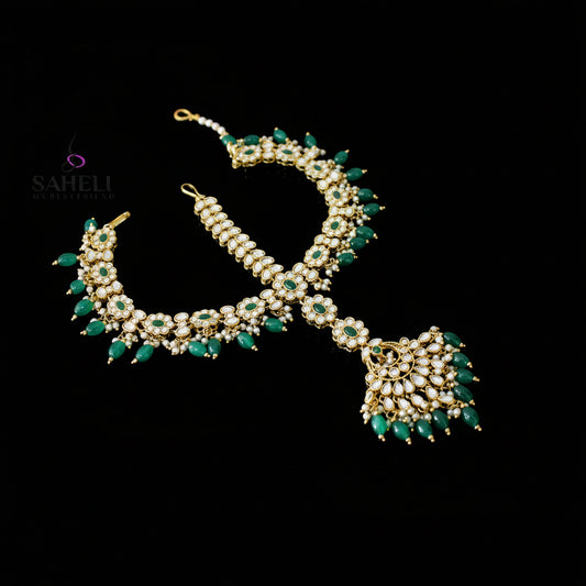 Jewelry set with necklace and bracelet featuring green stones on a dark background, branded 'Saheli'.