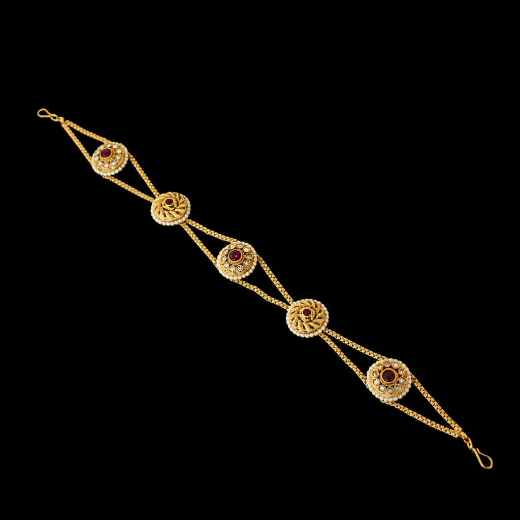 Gold bracelet with red stones on a dark background, featuring the brand 'Saheli'.