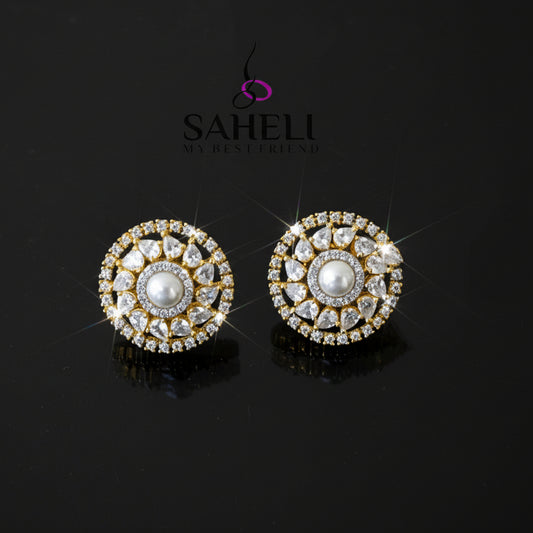 Pair of gold and diamond earrings on a dark background with 'Saheli' branding.