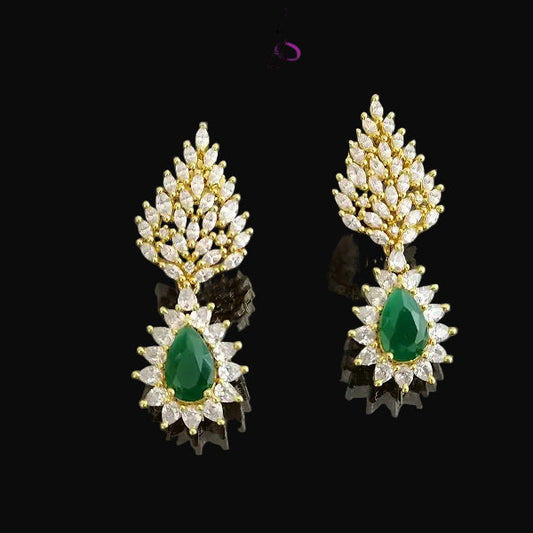 Gold and green gemstone earrings on a dark background with 'SAHELI' branding.
