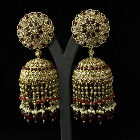 Pair of gold and red beaded earrings on a black stand against a black background