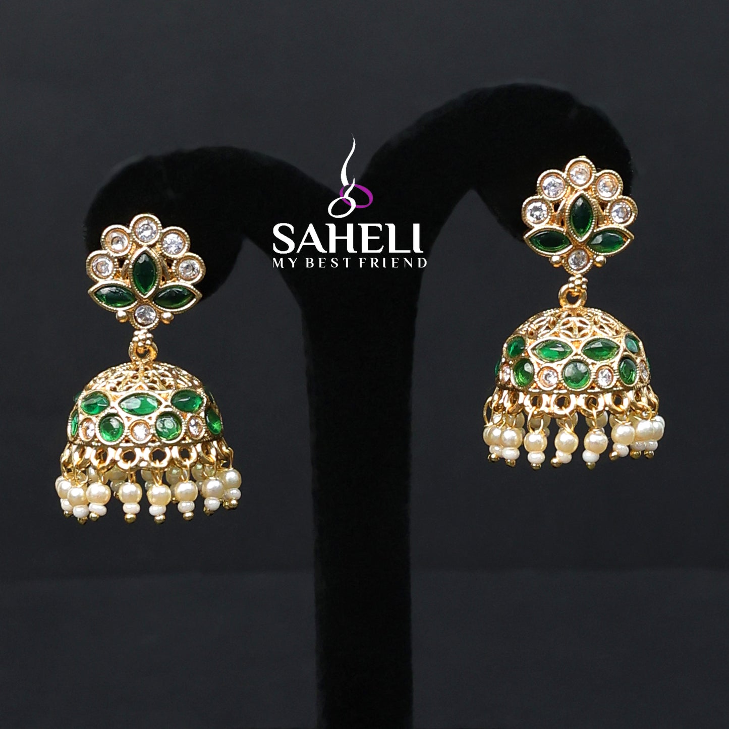Gold and green earrings on a black stand with 'Saheli' branding.