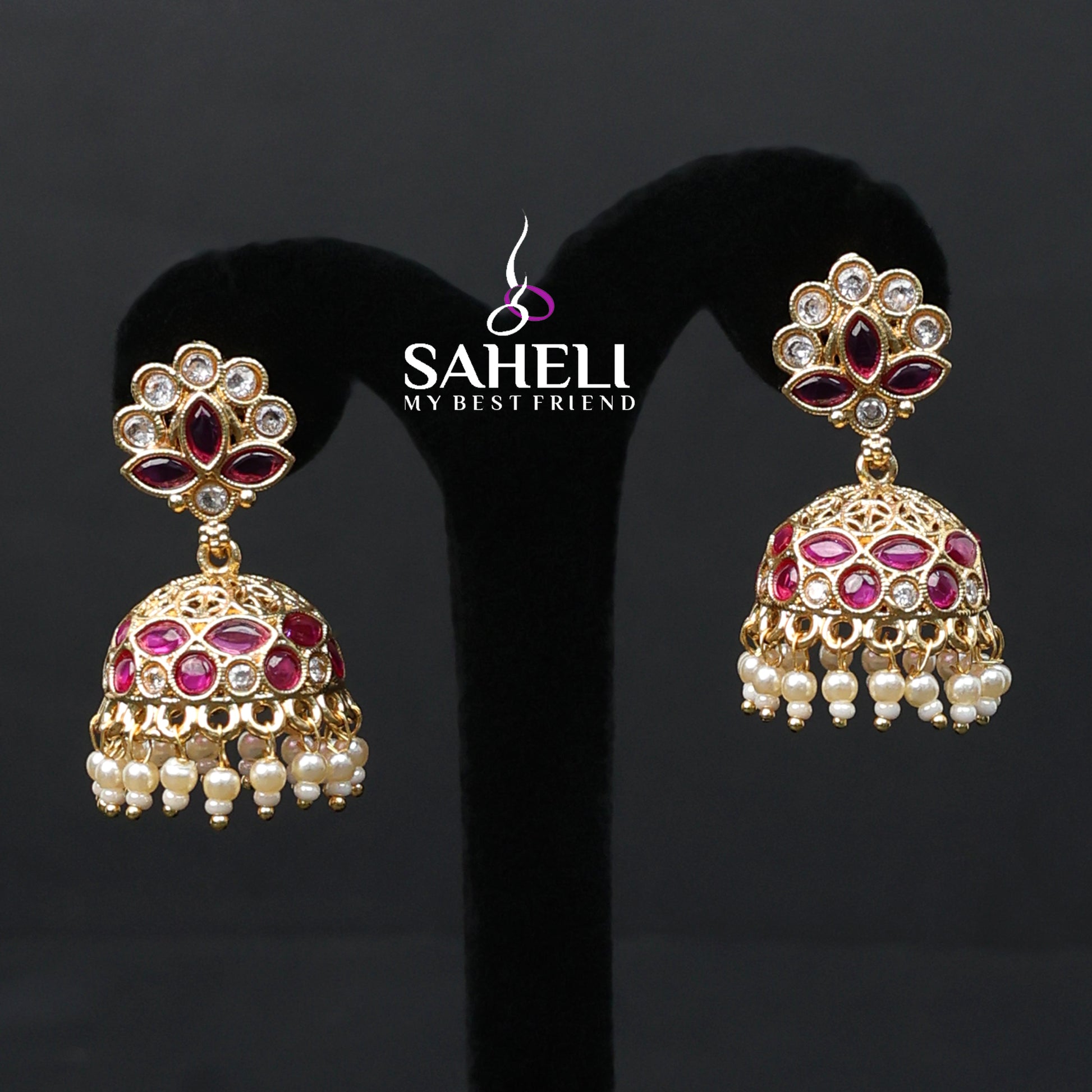 Gold and red gemstone earrings on a black stand with 'Saheli' branding.