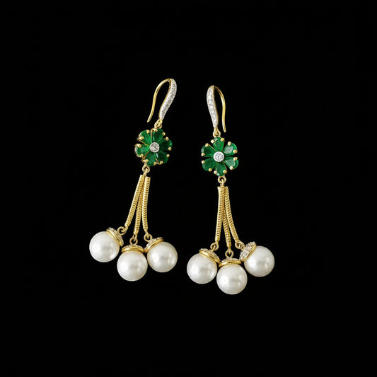 Pair of earrings with pearls and green gemstones on a dark background, branded 'SAHELI'.