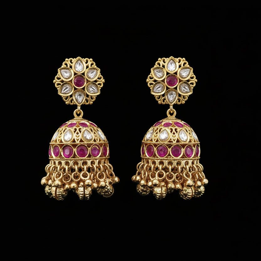 Gold earrings with red and white stones on a black stand, SJNX brand visible