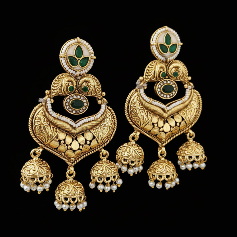 Ornate gold earrings with green and black accents on a textured black surface