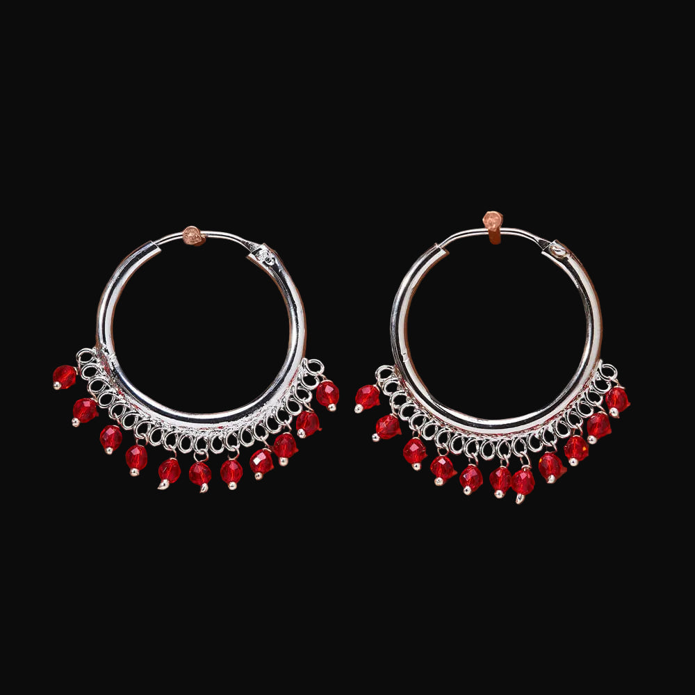 Pair of silver hoop earrings with red beads on a brown background