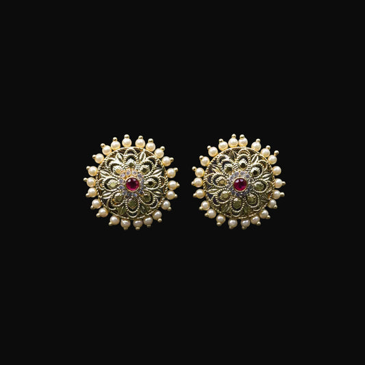 Gold earrings with red gemstones on a black stand, featuring the brand 'SAHELI'.