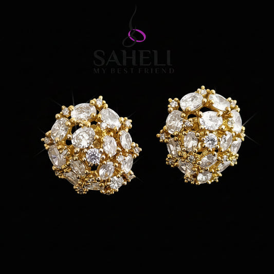 Gold and diamond earrings on a gray background with 'Saheli' branding.