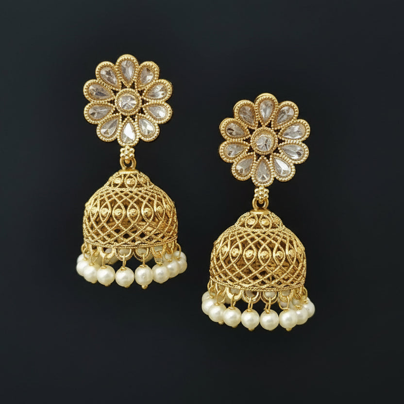 Gold earrings with floral top and ball-shaped bottom on a gray stand against a black background