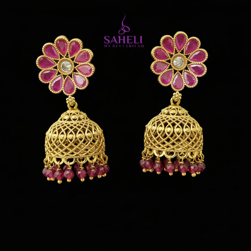 Gold and pink floral earrings on a gray stand with 'Saheeli' branding.