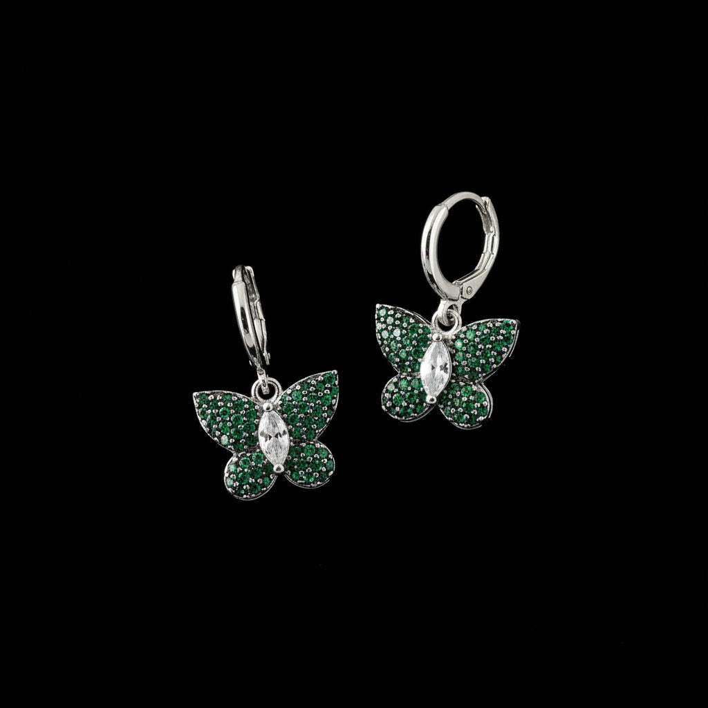 Butterfly-shaped earrings with green gemstones on a dark background, branded 'Saheli'.