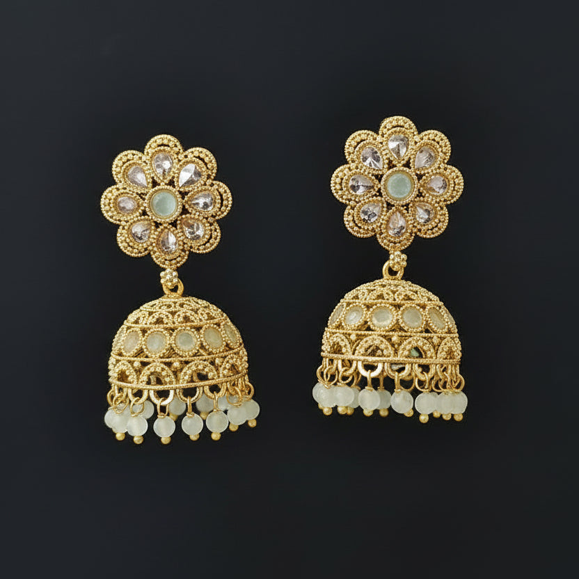 Gold floral earrings with intricate designs on a gray stand against a black background
