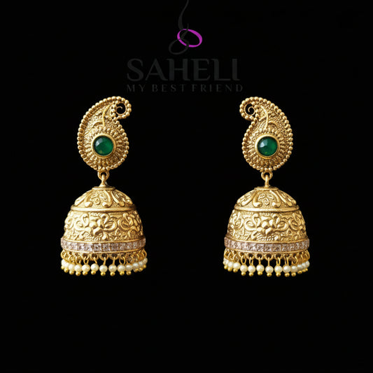 Gold earrings with green gemstones on a gray stand, branded 'Saheli'.