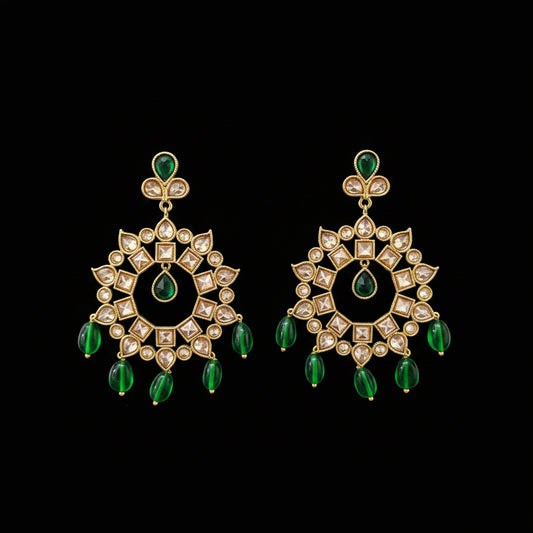 A pair of gold-toned Kundan chandelier earrings with green teardrop beads and clear stones, displayed on a gray Y-shaped stand against a gray background. The brand logo 'SAHELLI MY BEST FRIEND' is visible at the top.