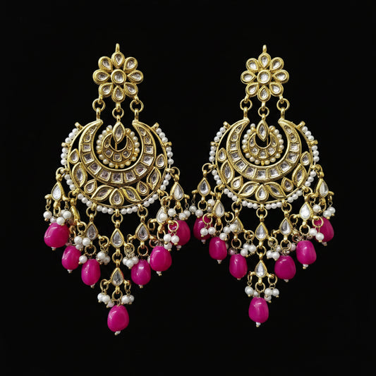 A pair of ornate gold-toned Indian chandelier earrings with white faux pearls and bright pink bead drops, displayed on a black stand against a dark gray background. The brand logo 'SAHELL MY BEST FRIEND' is visible in the top left corner.