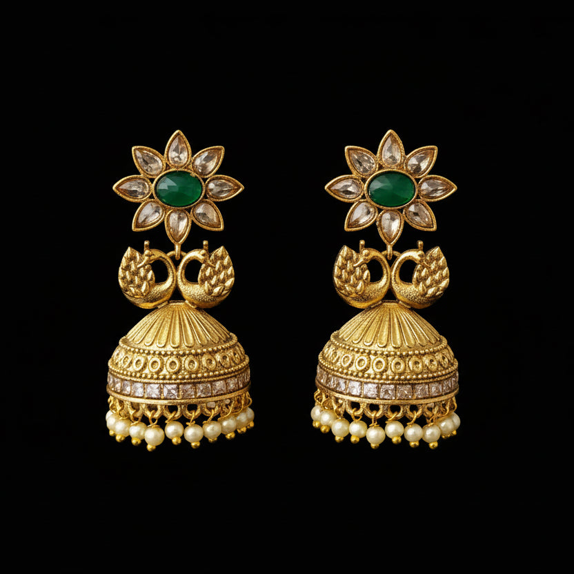 Gold earrings with green gemstones on a gray stand, branded 'SAHELI'.
