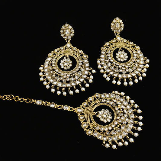 Ornate gold and pearl necklace with matching earrings on a dark background, featuring the brand 'Saheili'.