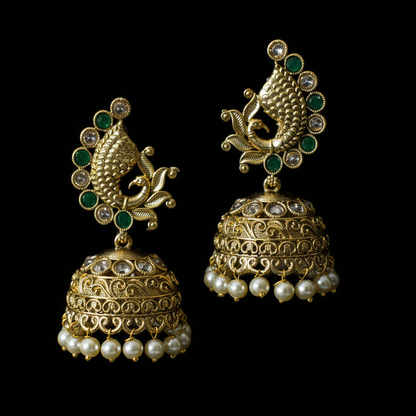 Gold and pearl jhumka earrings with green stones on a black background, branded 'Saheli'.