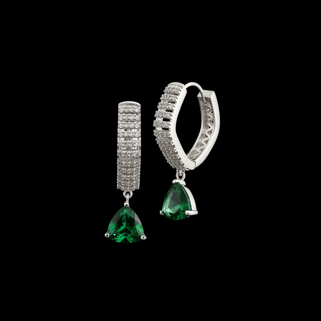 Pair of earrings with green gemstones and silver accents on a gray background, branded 'SAHELI'.