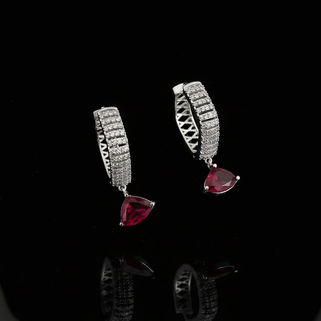 Silver earrings with red gemstones on a dark background, featuring the brand 'Saheli'.