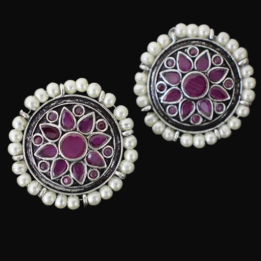 Pair of earrings with purple floral design and pearl accents on a dark background