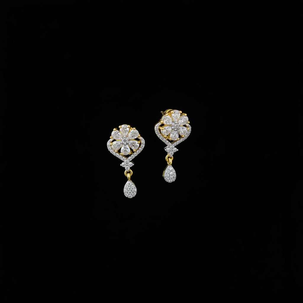 A pair of gold and silver drop earrings with clear pavé stones, displayed on a dark gray velvet jewelry cushion against a dark gray background.