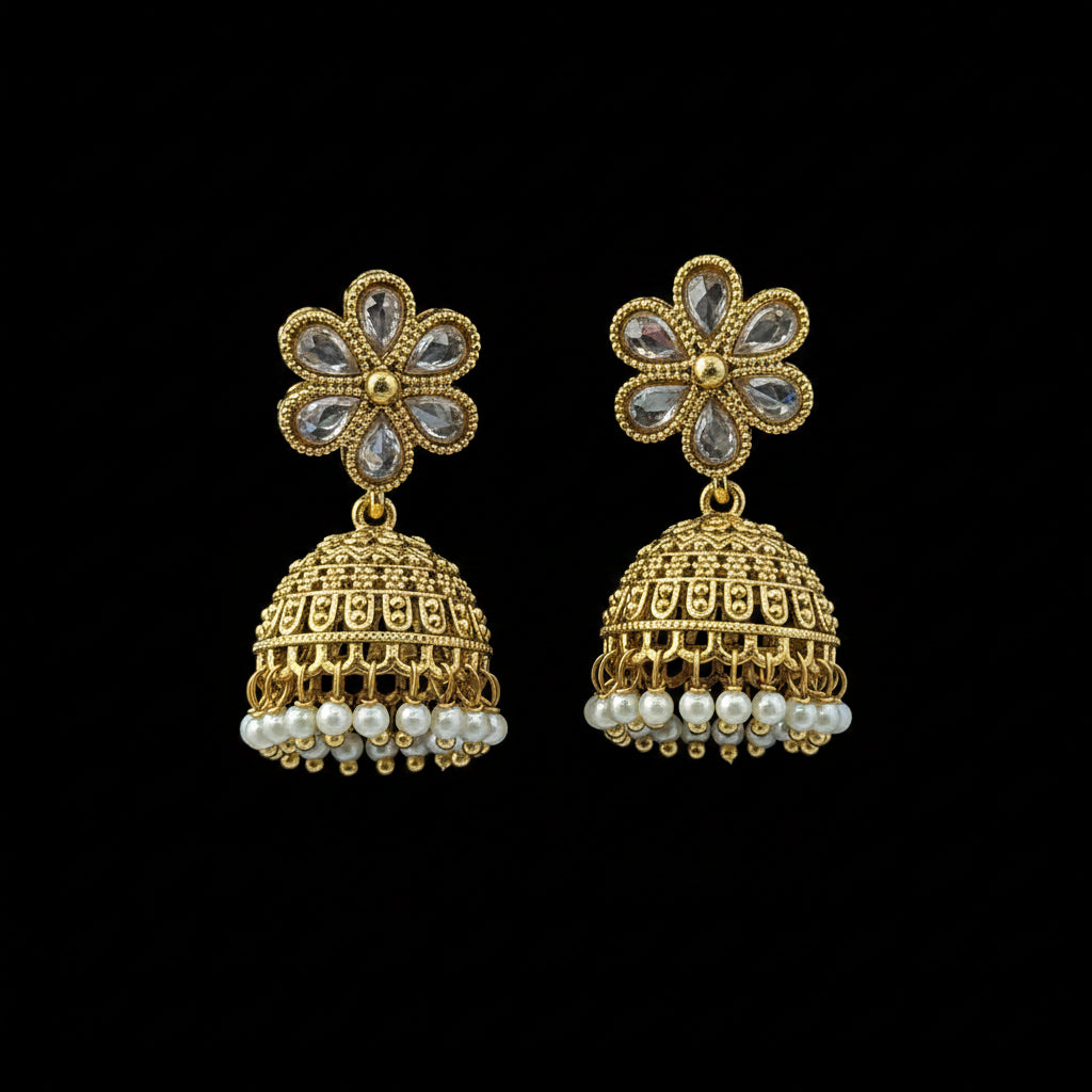 A pair of gold-toned Indian jhumka earrings with clear teardrop stones in the flower-shaped studs and small white pearl-like dangling beads, displayed on a textured blue background.