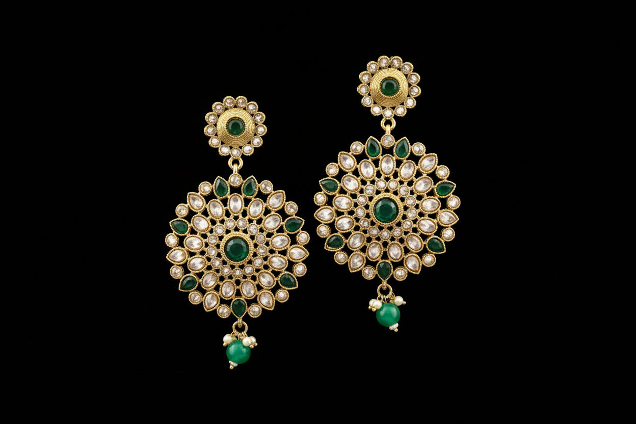 Gold and green earrings on a gray stand with 'Saheli' branding.