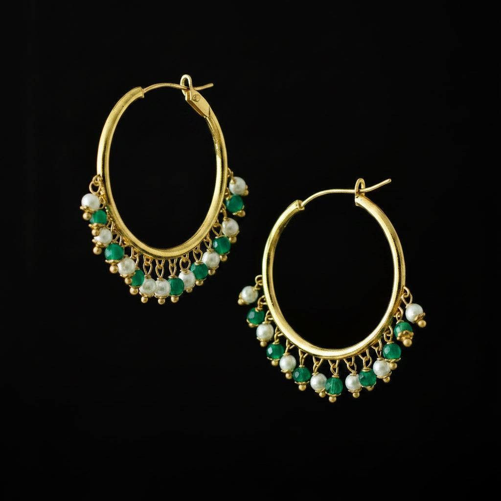 A pair of gold-plated hoop earrings with dangling chains of green and white beads, displayed on a dark reflective surface with the SAHeli brand logo above.
