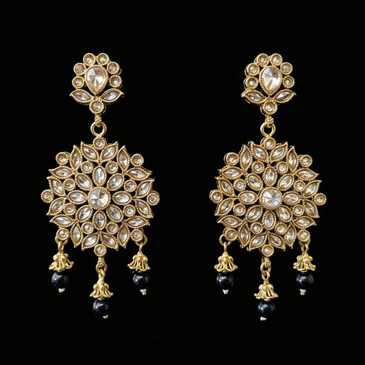 Gold and black earrings on a gray stand with 'SAHELI' branding.