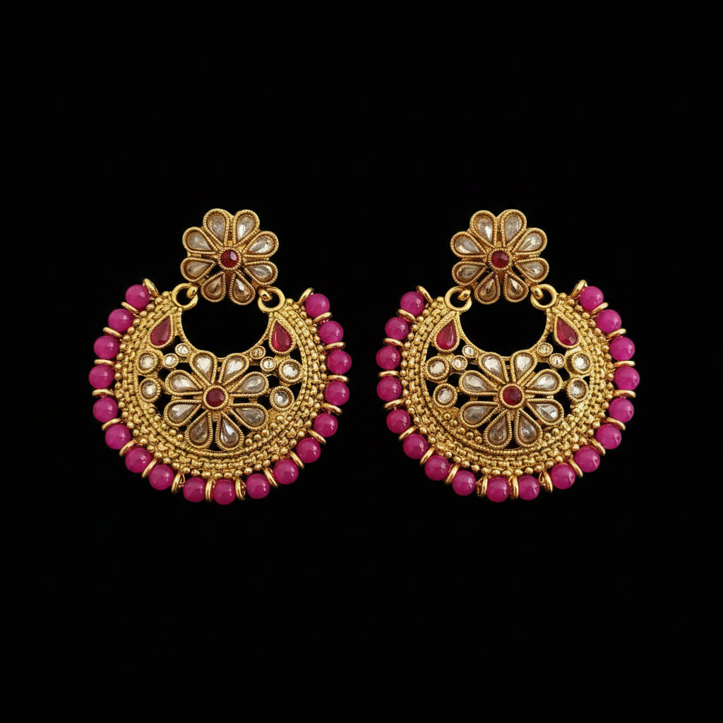 A pair of gold-toned Indian jhumka earrings decorated with pink beads and small clear stones, displayed on a dark gray reflective surface with the brand logo 'SAHELI MY BEST FRIEND' at the top.