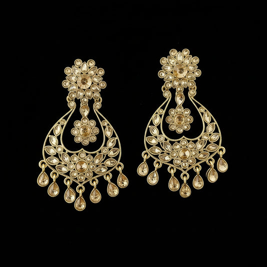A pair of ornate gold-toned Indian chandelier earrings embellished with clear teardrop-shaped crystals, displayed on a dark reflective surface with a 'SAHELI MY BEST FRIEND' logo watermark at the top.