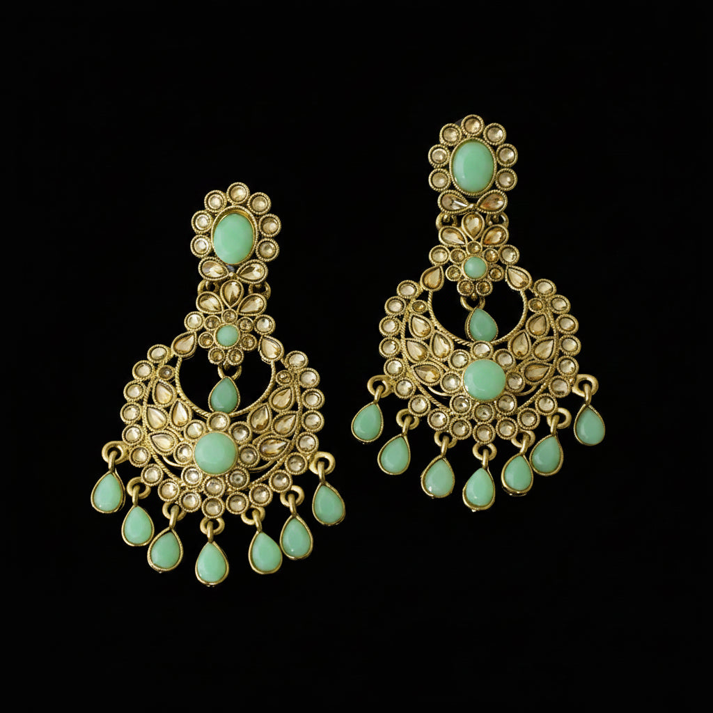 A pair of gold-toned Indian chandbali earrings with mint green stone accents, displayed on a dark reflective surface. The brand logo 'SAHELI MY BEST FRIEND' is visible in the top left corner.