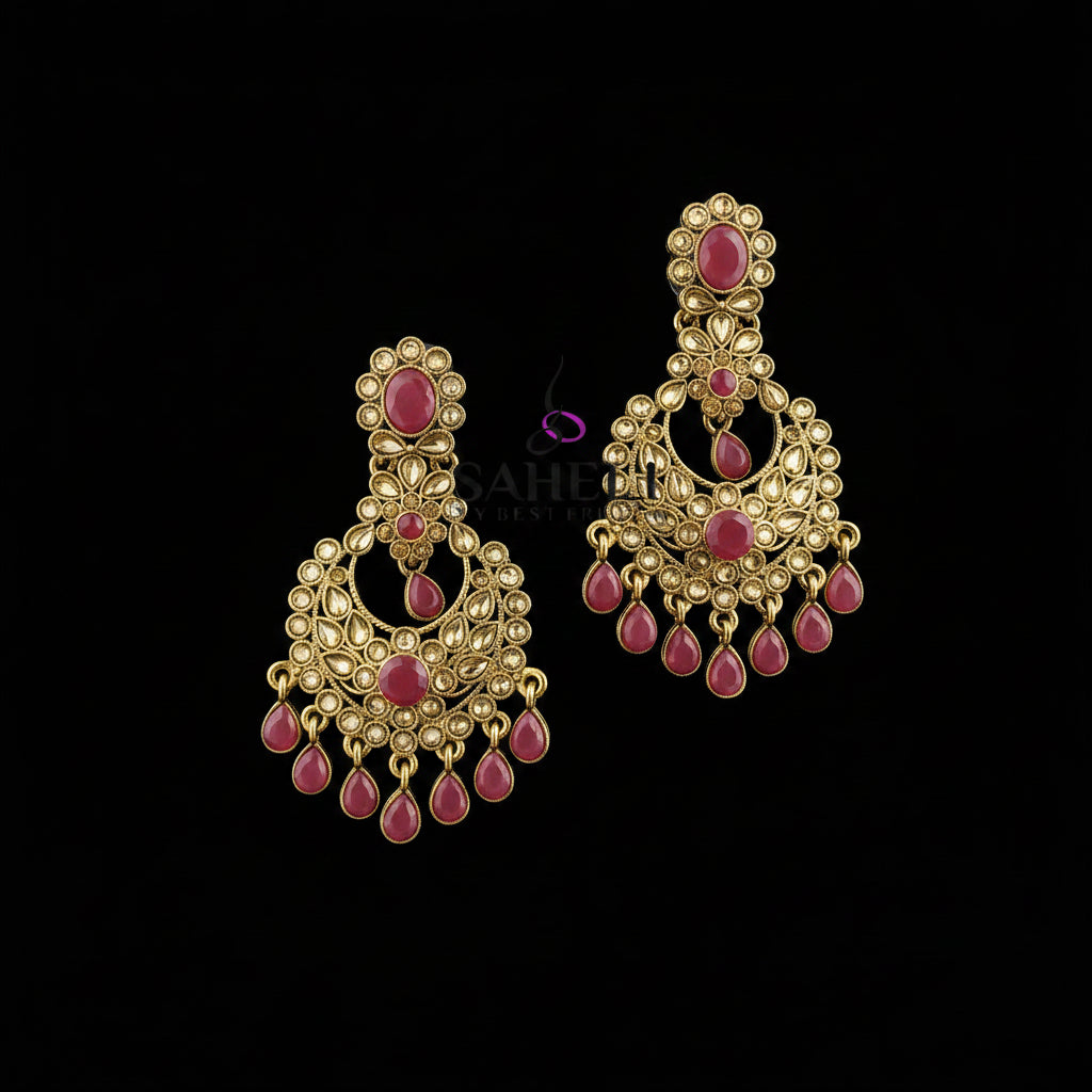 A pair of gold-toned traditional Indian chandbali earrings with pink gemstone accents, displayed on a dark reflective surface with the SAHELI MYBESTFRIEND brand logo at the top.
