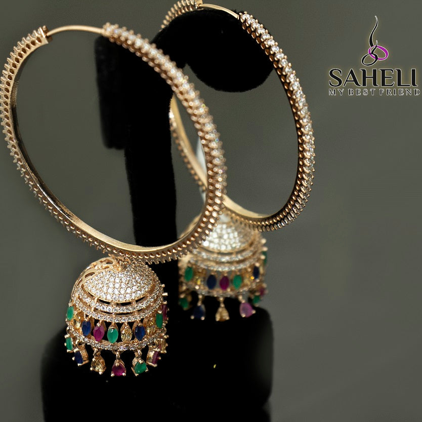 Gold hoop earrings with intricate designs and colorful gemstones on a black stand, branded 'Saheli'.