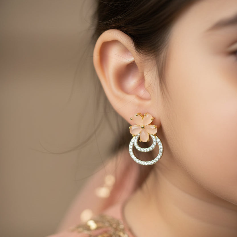 Pair of floral earrings with circular designs on a gray cushion against a dark background