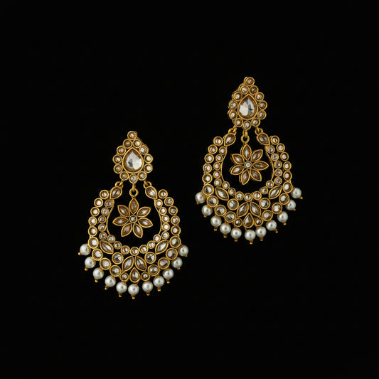 A pair of ornate gold-toned traditional Indian chandelier earrings decorated with white faux pearls and small clear stones, displayed on a dark reflective surface. The brand logo 'SAHELI MY BEST FRIEND' is visible in the top left corner.