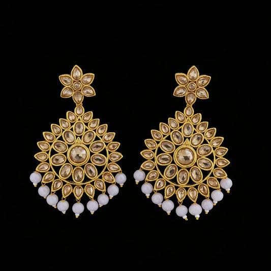 A pair of gold-toned Indian Kundan chandelier earrings with clear teardrop crystals and white bead fringe, displayed on a dark reflective surface with the SAHeli My Best Friend logo at the top.