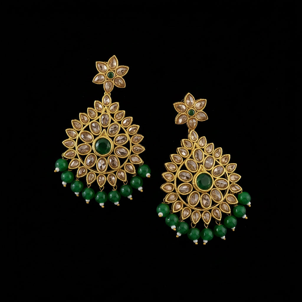 A pair of gold-plated Indian chandbali earrings decorated with green stones and clear crystals, displayed on a dark reflective surface with the brand name SAHELI MY BEST FRIEND at the top.