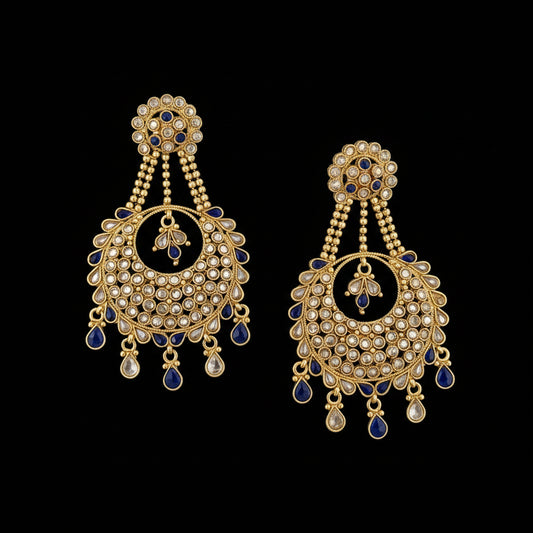 A pair of gold-toned Indian chandbali earrings embellished with clear crystals, blue enamel, and small blue stone drops, displayed on a dark gray reflective surface. The brand logo 'SAHELI MY BEST FRIEND' is visible at the top center.