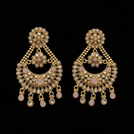 A pair of gold-toned Indian chandbali earrings embellished with clear crystals and light pink stones, displayed on a dark gray reflective surface with the 'SAHELI MY BEST FRIEND' logo at the top.